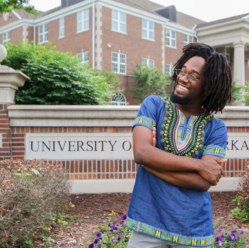 Man stands in front of the University of Central Arkansas rocking freeform dreads in a traditional African shirt