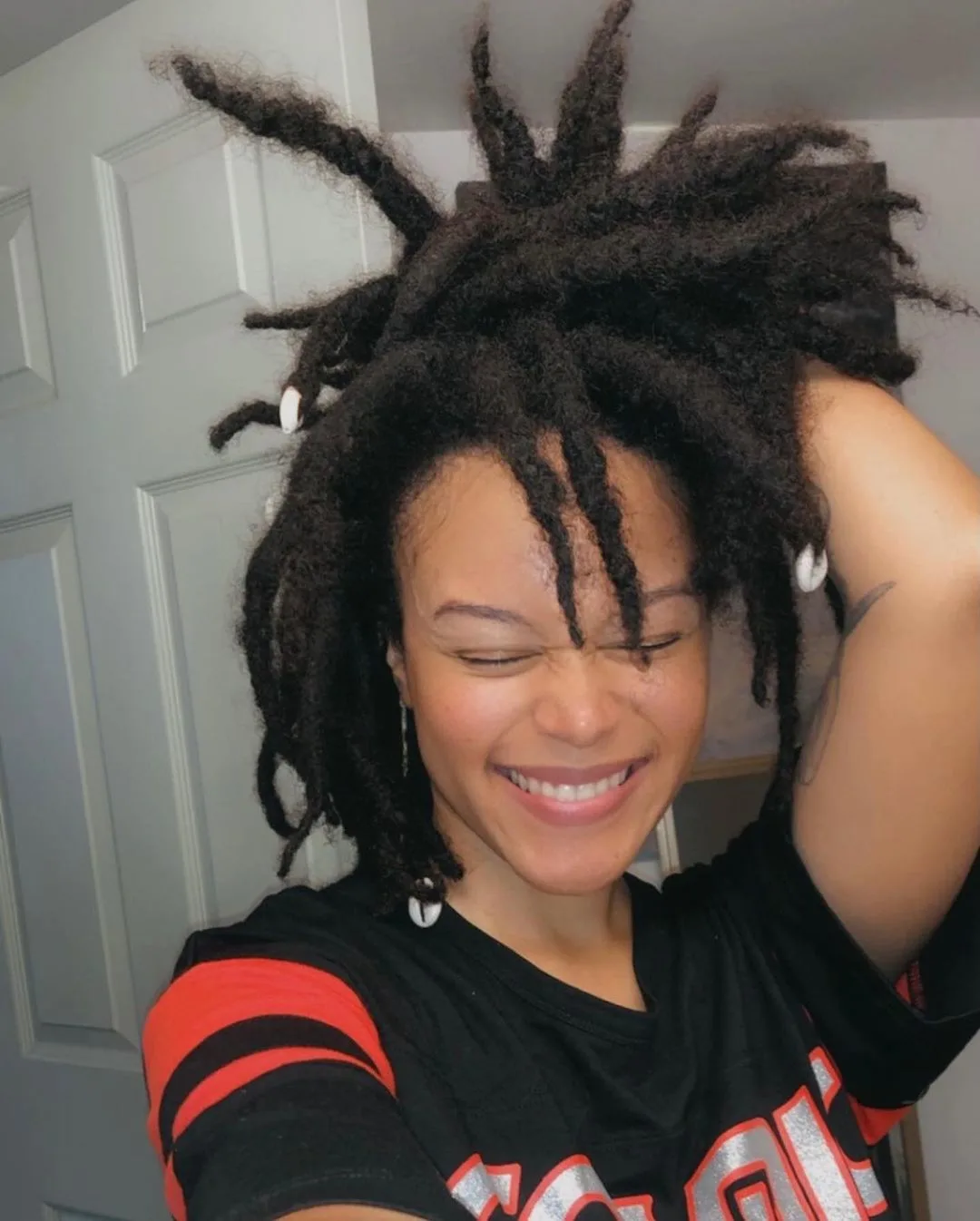Lady with spikey dreadlocks smiles and does a crazy party face while wearing a bright colored shirt