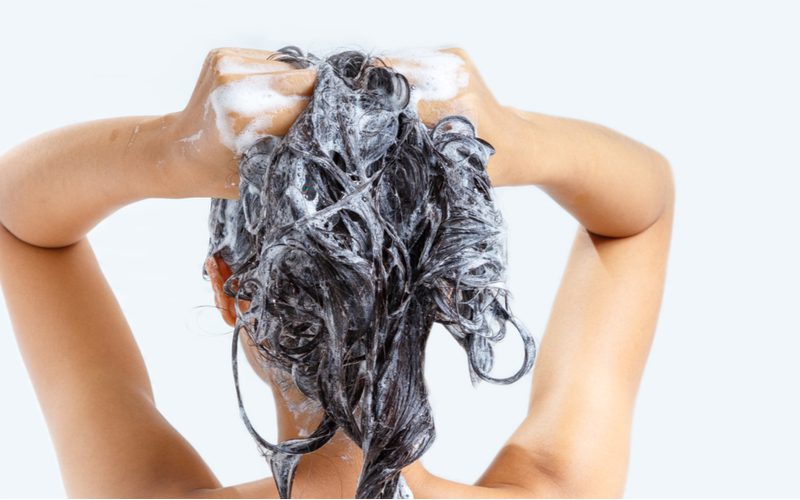 Woman standing in the shower shampooing her hair for a piece on how to get rid of frizzy hair