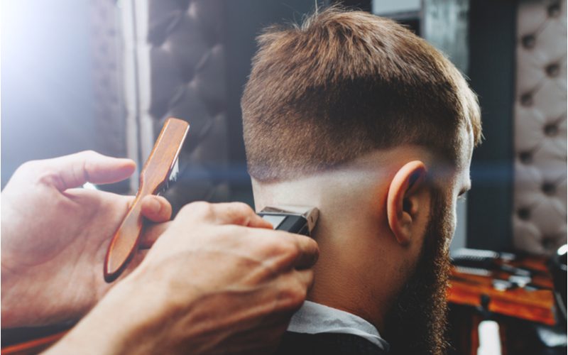 Young man with a hard-lined layered undercut gets his neckline trimmed up by a barber with a razor and a brush