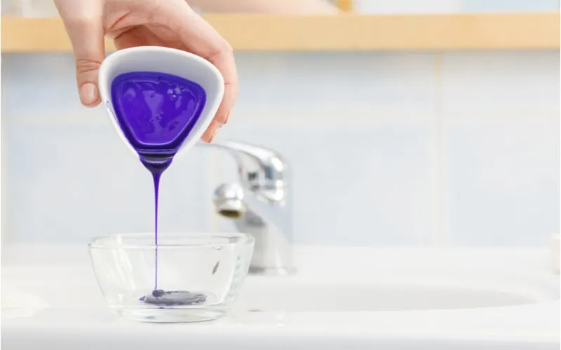 Hand pouring purple shampoo into a glass bowl to help get rid of brassy hair