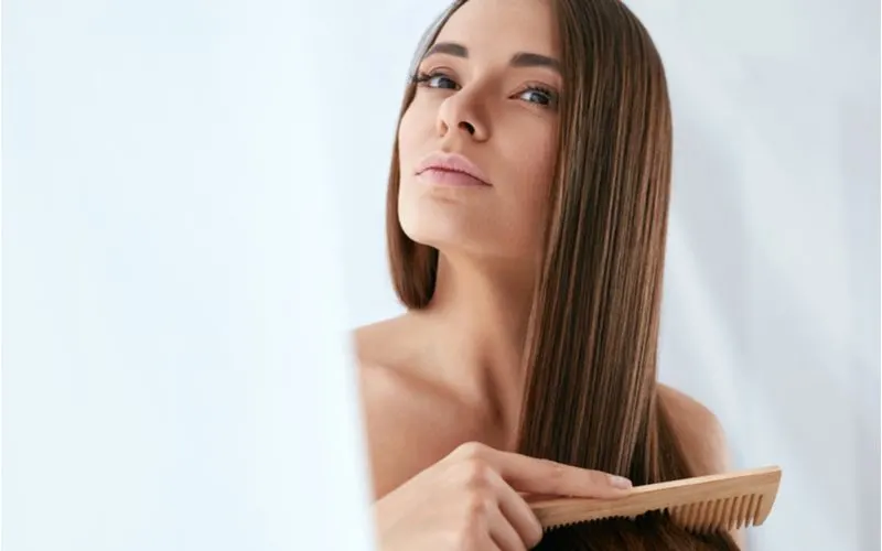 Euro woman with a wooden comb pulls it through her hair while looking up and to the left