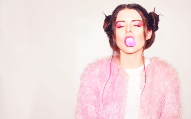Girl with crazy space buns in a pink boa pops her pink gum with pink lips