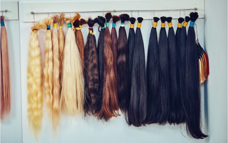 Bunch of hair extensions in various colors hanging on a door to illustrate a step on how to do box braids on yourself