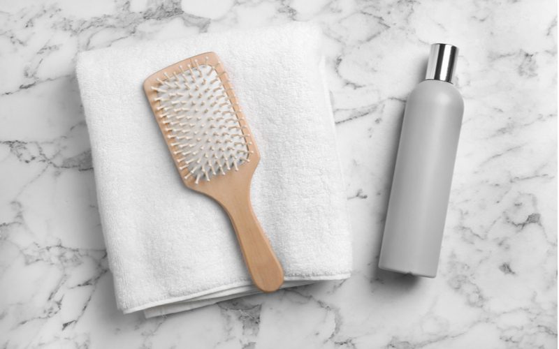 To help symbolize how to clean a hair brush, a bamboo brush sits on a towel next to a shampoo or cleaning solution