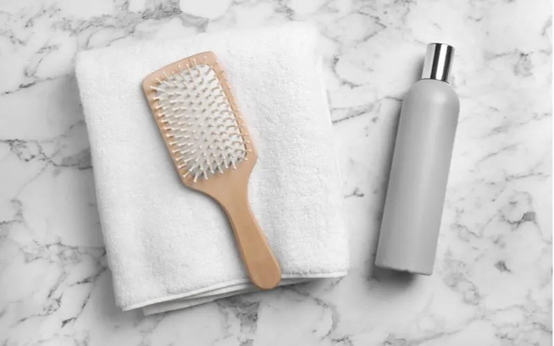 To help symbolize how to clean a hair brush, a bamboo brush sits on a towel next to a shampoo or cleaning solution