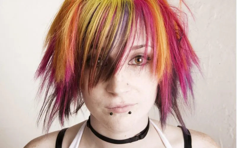 Close up of a girl with multi-colored emo hair in pink and orange with snake bit piercings looking at the camera 