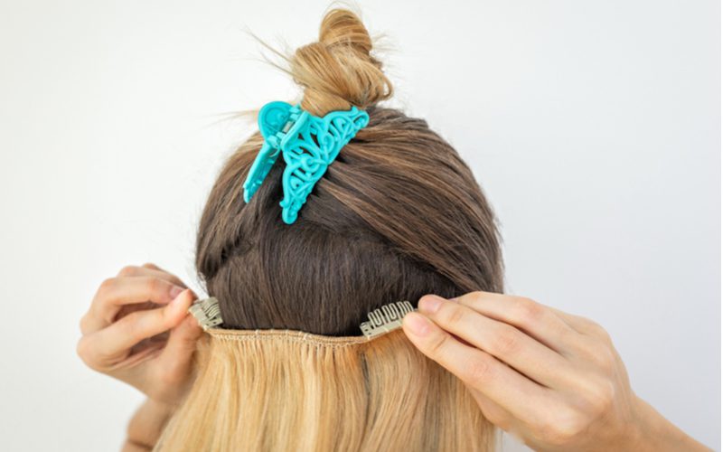 Lady with clip-in hair extensions has her hair up in a bun and the bun clipped by a teal clip