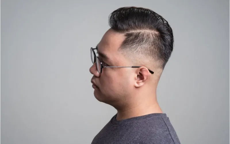Young Asian man wearing glasses wears an undercut fade with a hard part on his left side and combs his hair to the right