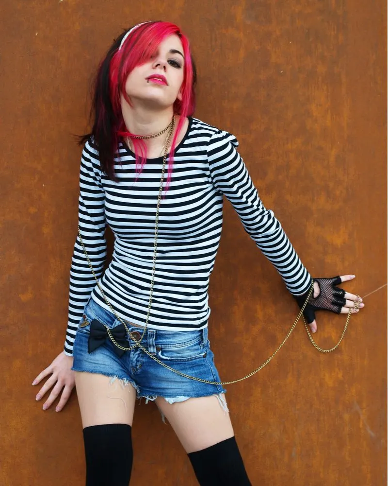 Pale skinned emo teen in a black and white striped shirt with a chain around her neck wearing a glove and thigh-high socks
