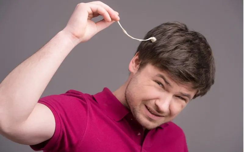 Man with a bunch of chewing gum in his hair pulls it from his head and winces