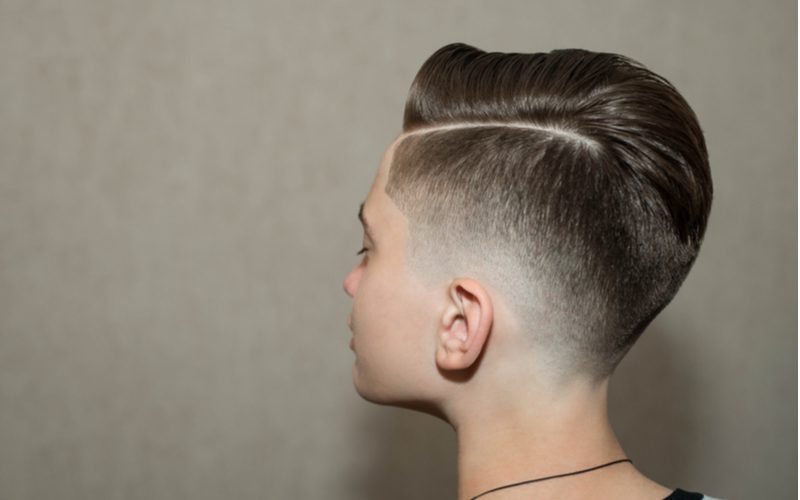 Young teenage boy with a retro undercut fade haircut stands in a grey studio looking left
