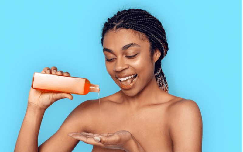 Gal with braids in a blue room pours the best shampoo for oily hair into her hand