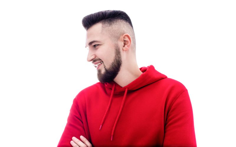 man in a red hoodie wearing a high undercut fade in a room crossing his arms and smiling