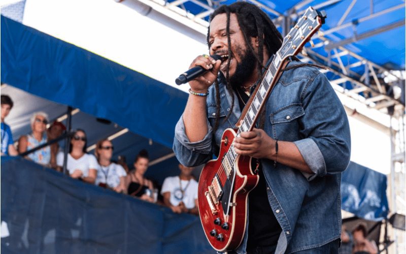 Image of Steven Marley singing into a microphone and holding a guitar while rocking freeform dreads