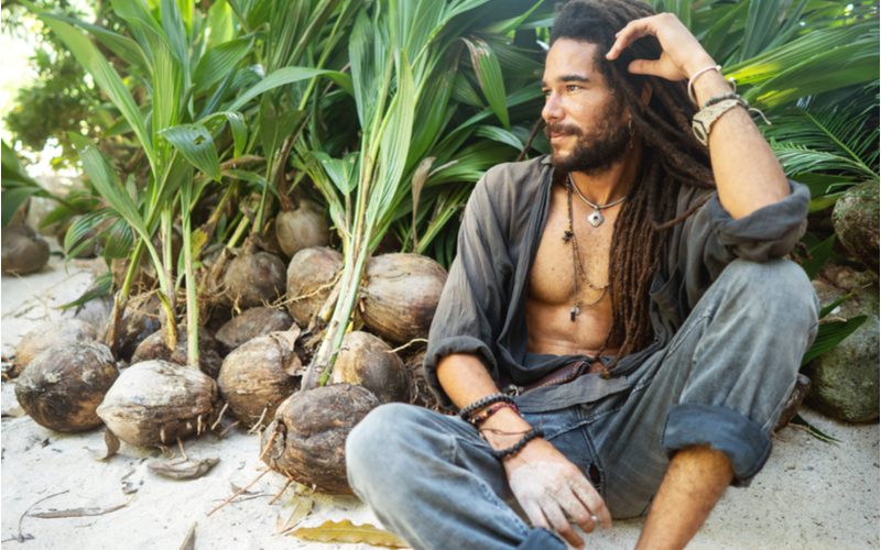 Man who just learned how to free form dreads sits on a beach with his hand in his hair