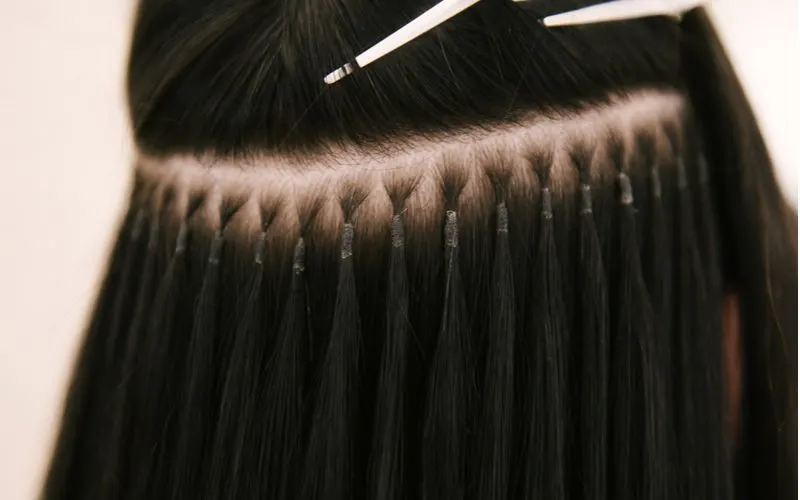 Gal with i-tip/microlink extensions gets them in a close-up image featuring brunette hair and a metal probe