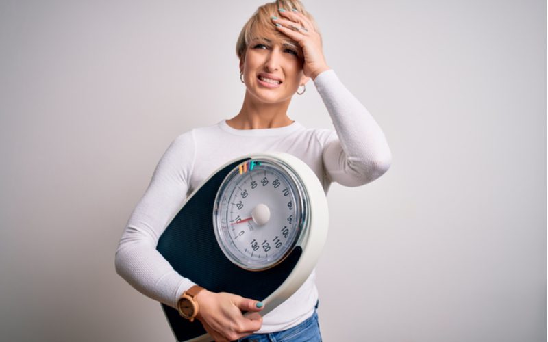 Woman holding a scale in one hand and her hair in another for a piece on how much does hair weigh