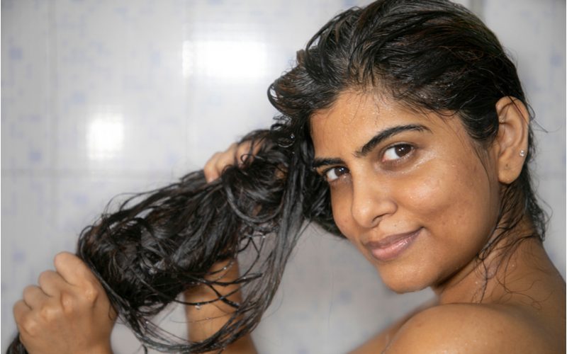 Indian gal removing moisture out of her hair while looking to the left in the shower for a piece on how to dry curly hair