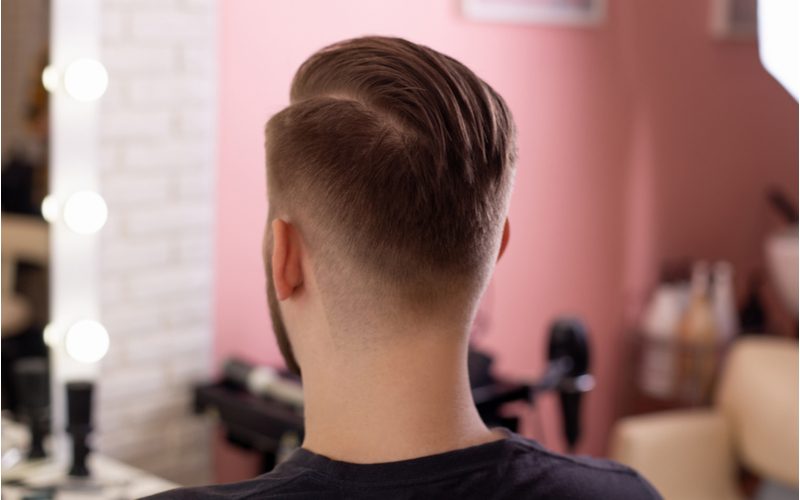 Man with a side part undercut fade looks toward the mirror in a barber shop while sitting down
