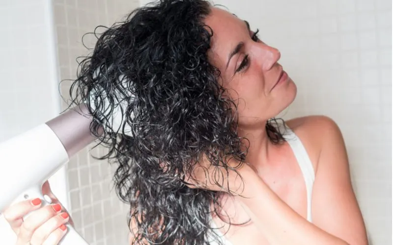Curly haired woman using a hair diffuser and holding her curls