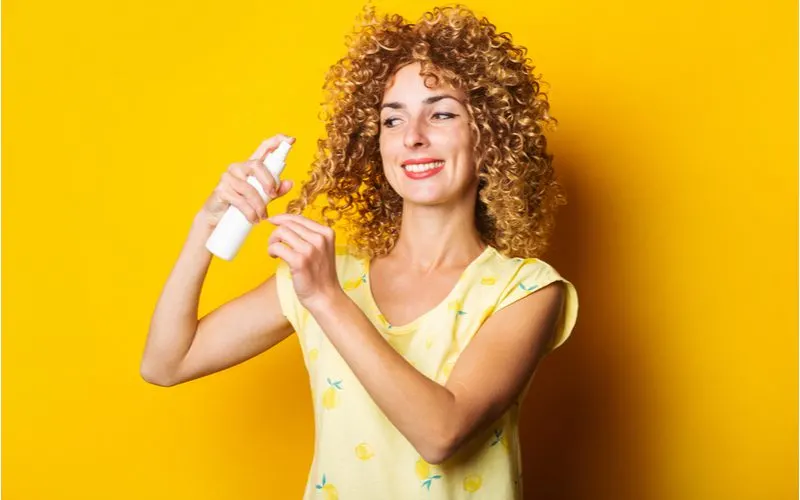 Happy woman spraying her hair with hair spray for a piece on how to get rid of frizzy hair