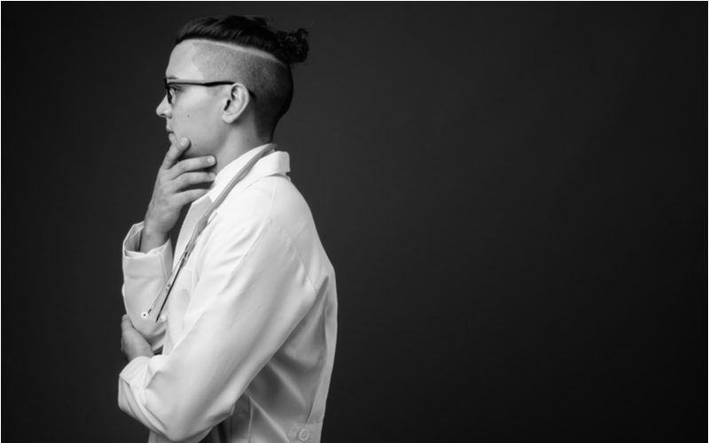 Disconnected undercut fade inspiration on a guy in an oversized white shirt in a black and white image in a black studio