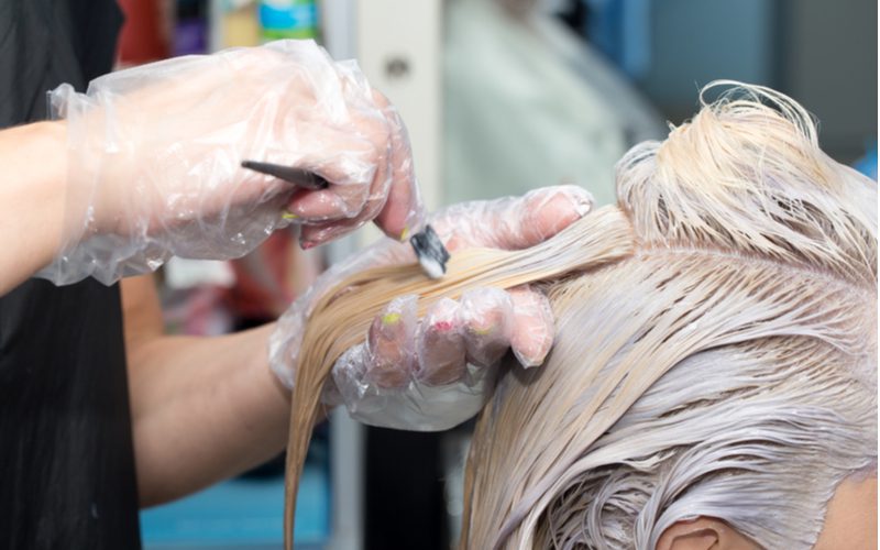 Để minh họa cho việc bạn nên để thuốc tẩy trên tóc trong bao lâu, một người phụ nữ đeo găng tay vẽ tóc của một người phụ nữ trong tiệm