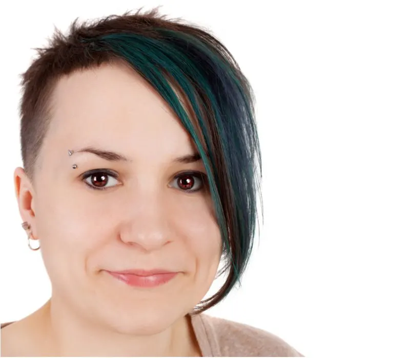 Teen girl with purple emo hair that's shaved on the left side grins with an eyebrow ring in a white room