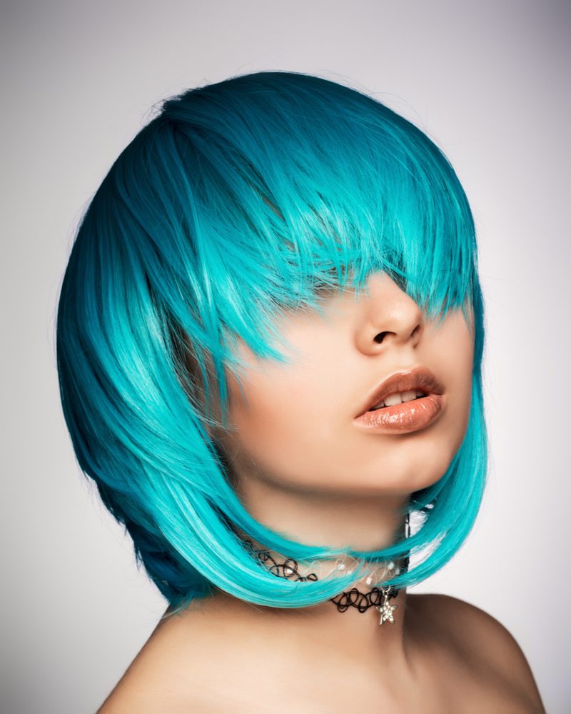 Girl with green and teal emo hair letting it fall on her face above her eyes wearing a choker and no top