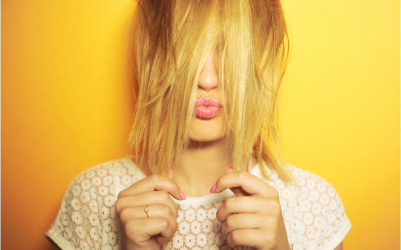 To highlight how to get rid of brassy hair, a woman with yellow hair pulls it in front of her face and makes the duck face pose with her lips