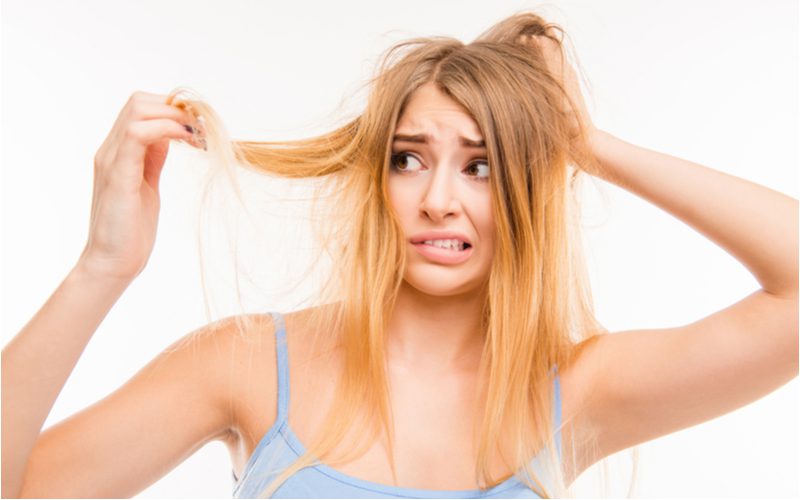 Để minh họa điều gì sẽ xảy ra nếu bạn để thuốc tẩy trên tóc quá lâu, một người phụ nữ tóc vàng đang giữ phần đuôi tóc bị hư hỏng và cháy của mình