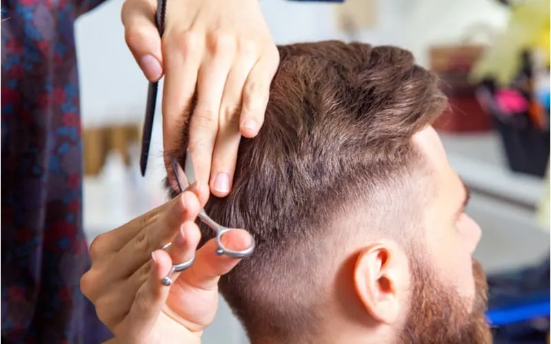 Man in a stylist's chair getting a low fade undercut with shears and a comb