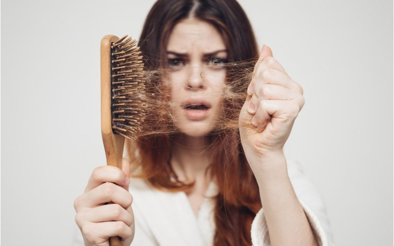 Đối với một phần về cách làm sạch bàn chải tóc, một người phụ nữ cầm bàn chải bằng một tay và dùng tay kia kéo tóc từ bàn chải