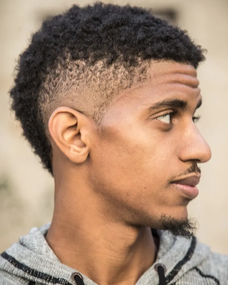 Man with an afro undercut fade wears a grey hoodie and looks left
