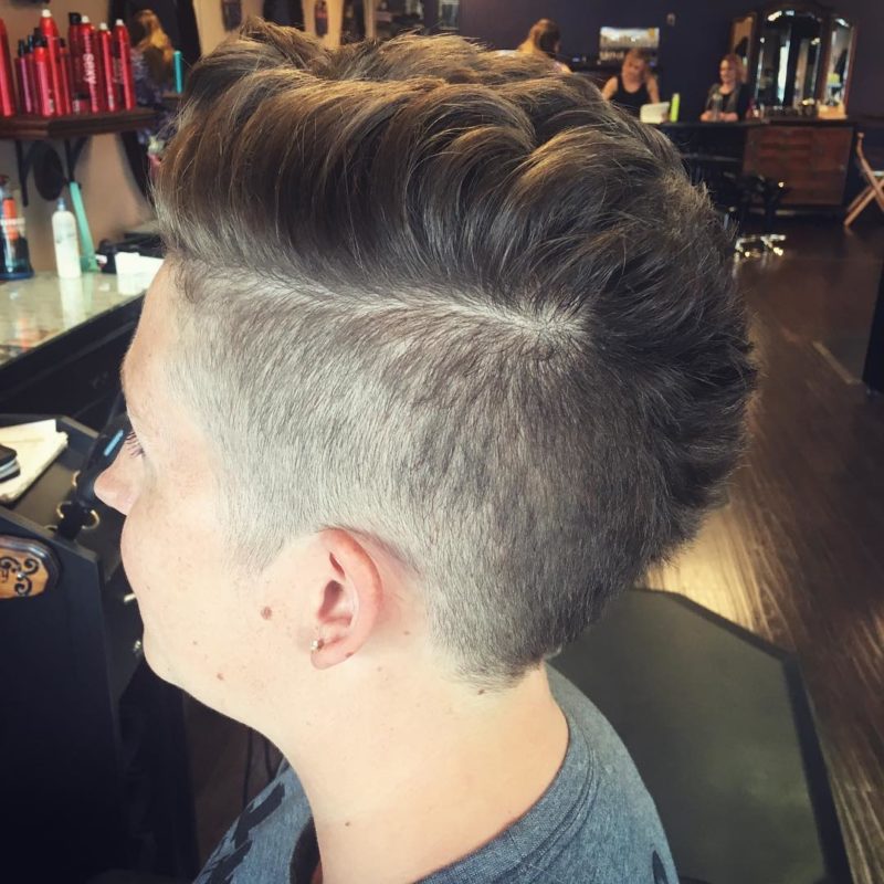 Gal with a fluffy female mohawk and a hard shaved part looking ahead in the salon chair
