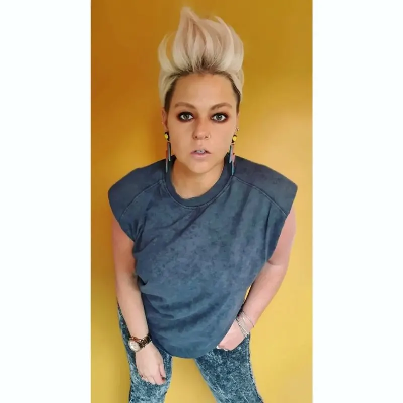 Female mohawk inspiration on a woman in a yellow room wearing a cutoff putting her left hand in her pocket