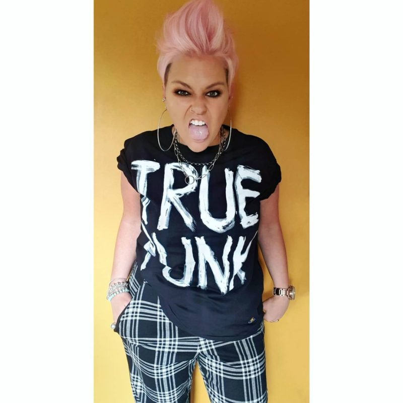 Woman with a pink female mohawk in a true punk shirt wearing chucks and checkered pants
