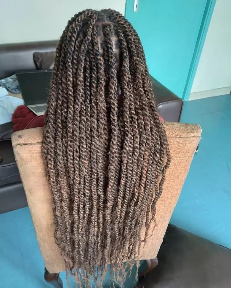 Woman with long kinky twists lets them flow over a tan chair while sitting in a living room