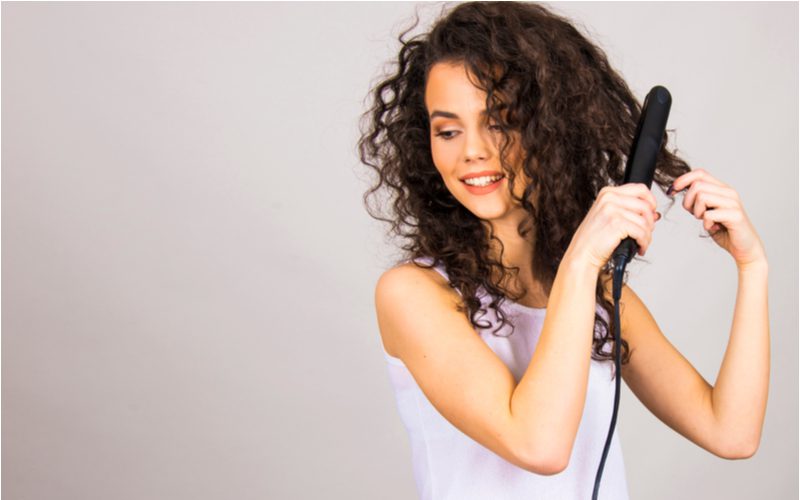 Woman with long curly hair and a flat iron in a studio showing us how to straighten curly hair