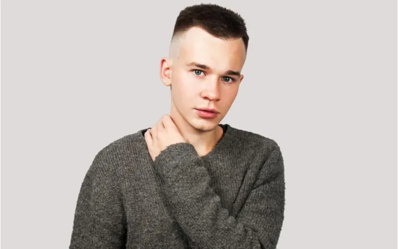 Man in a grey sweater rocks a long buzzed fade and holds his right shoulder