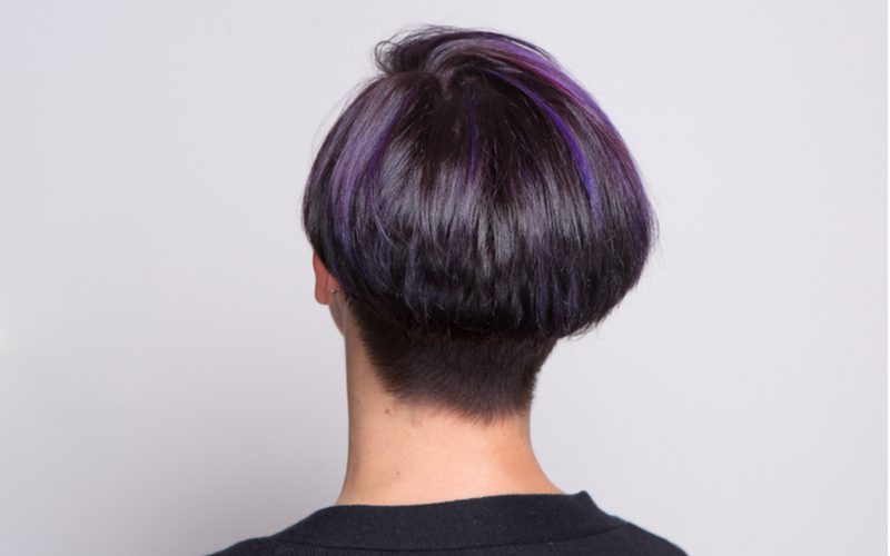 Modern mushroom bob haircut with purple hair streaks on a woman looking toward a wall