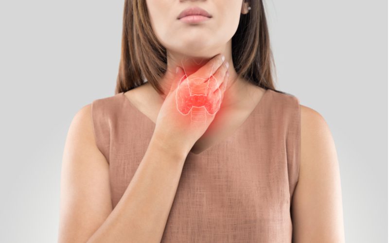 Woman holding her thyroid on the outside of her neck for a piece on factors that cause grey hair