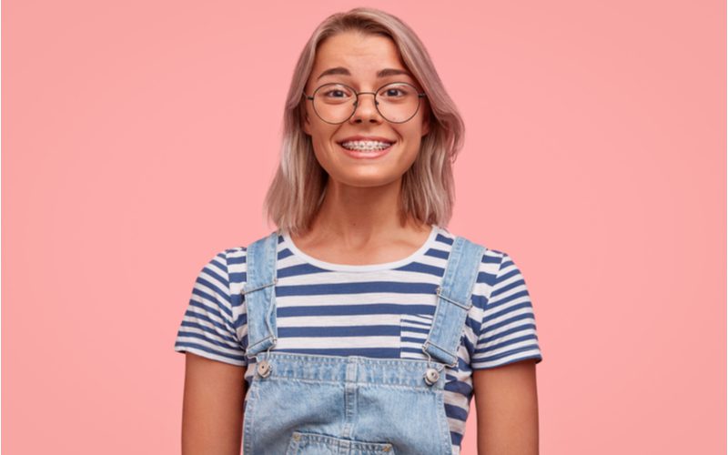 Lob With Cheekbone-Length Bangs on a woman standing in front of a pink background in overalls