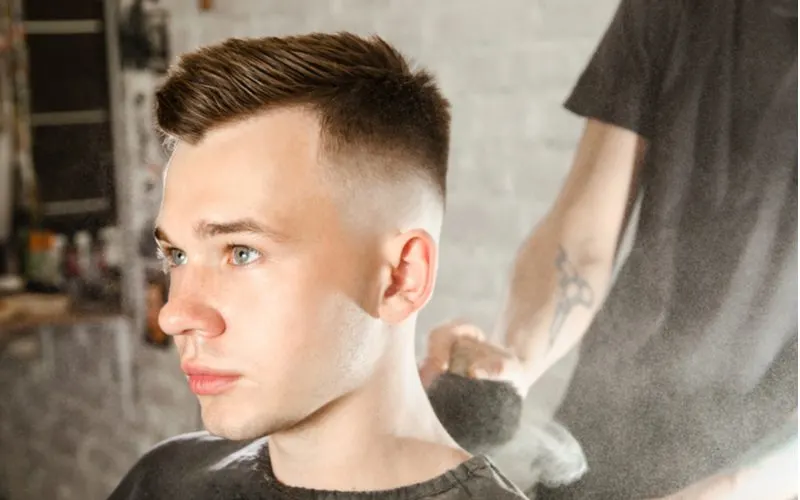 Man with a spiked haircut on top with a lot drop fade sits in a barber chair