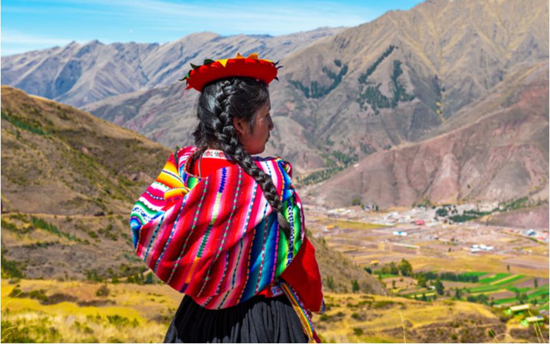 Peruvian woman standing in a mountain range looking over a city below