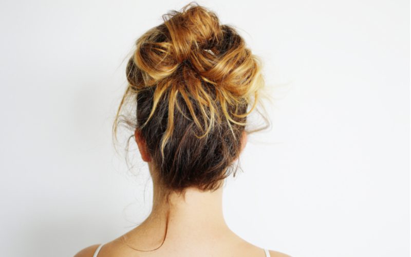 Messy bun as an easy everyday hairstyle on a woman looking toward a white wall