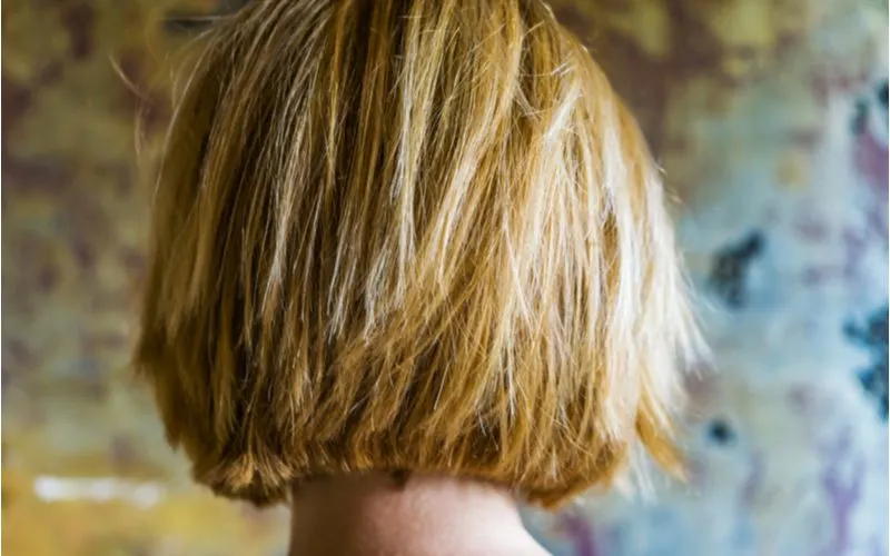 Messy texture layered bob haircut on a woman standing in front of a camo-looking wall
