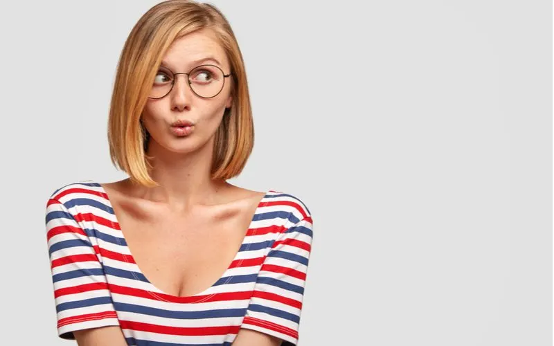 Cute girl with a bob haircut in a red and blue striped shirt puckers her lips and looks to the left