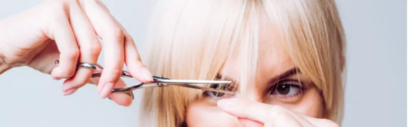 Woman cutting curtain bangs with blonde hair and scissors